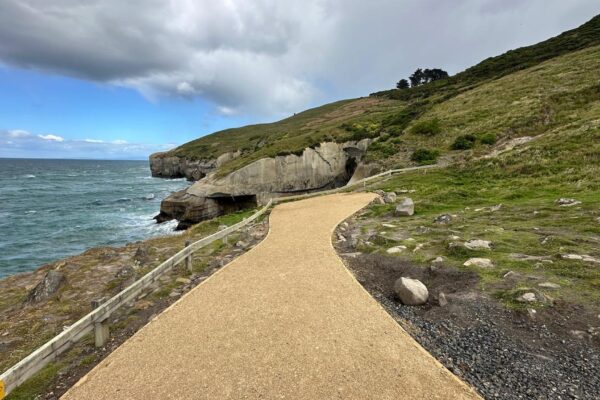 Completed coastal walking track beside rocky cliffs and ocean views, with a compacted gravel path and safety fencing. This recreation construction project includes civil construction, erosion control and siteworks to support safe public access.