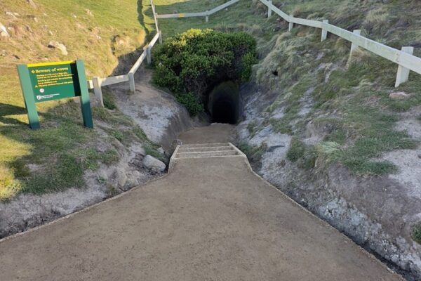 Completed walking track construction leading down through a coastal valley with fencing, compacted gravel surfacing and stone edging. The image shows recreation construction, erosion control, siteworks and civil construction in a rugged coastal landscape.