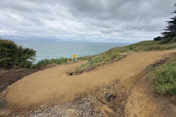 Walking track construction forming a compacted gravel path beside a coastal hillside and ocean views. The image shows civil construction, recreation construction, erosion control and site preparation for safe public access in a coastal environment.
