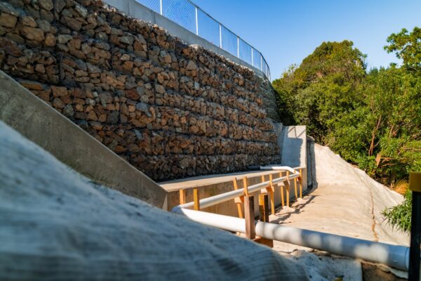 Large scale retaining walls and gabion baskets forming a reinforced concrete structure beside a steep accessway. This civil construction project includes siteworks, ground stabilisation and slope retention as part of a complex construction project.