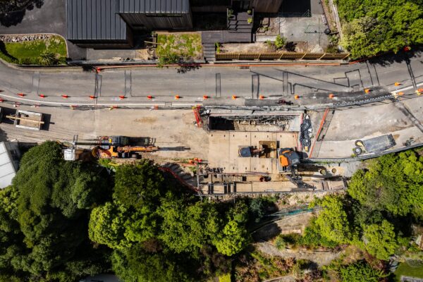 Aerial view of excavation, retaining walls and civil construction machinery working along a narrow hillside road. The project shows detailed site preparation, project management and site construction for a complex slope retention project.