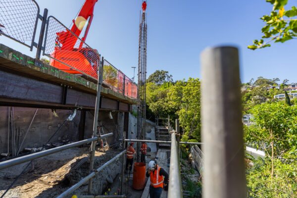 Crane lifting equipment for retaining walls and civil construction work on a narrow hillside site with scaffolding and safety fencing. The project involves excavation, slope retention and structure construction completed by skilled civil contractors.