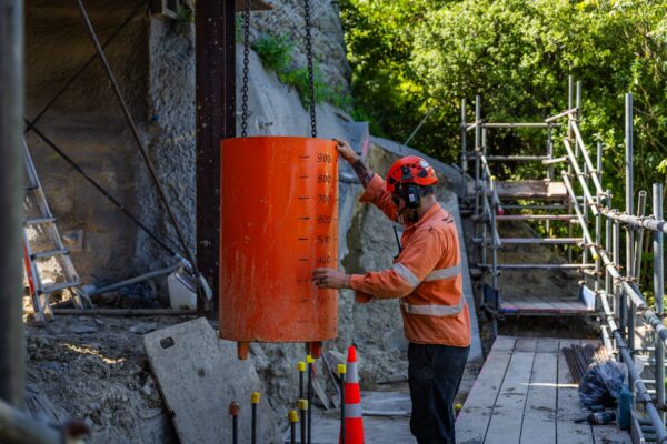 Construction worker guiding a suspended concrete section during sling operations on a retaining walls and civil construction site. The work shows careful project management, site construction and utility infrastructure support in a confined hillside location.