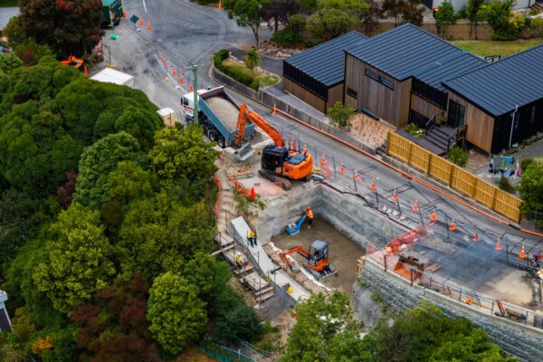 Aerial view of a civil construction site with excavation, retaining walls and machinery working alongside a hillside residential area. The project demonstrates project management, siteworks and complex construction projects delivered by civil works contractors.