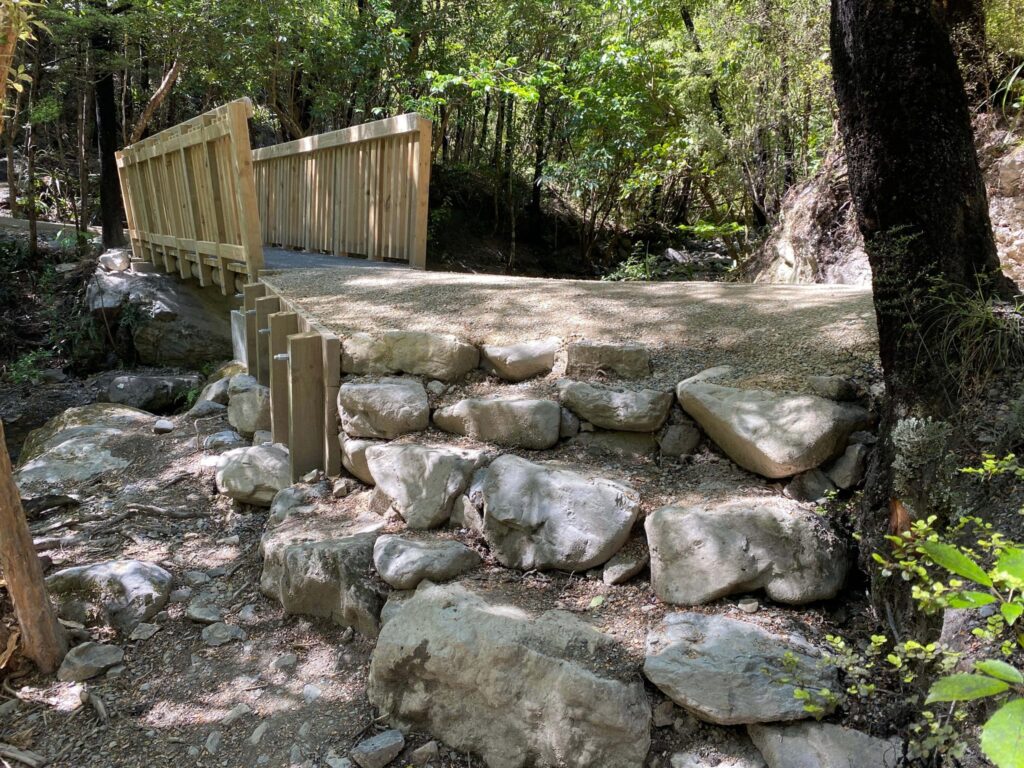 Timber bridge and rock retaining structure built beside a forest stream as part of recreation construction and walking track construction. The image shows civil contractors completing bridge construction, timber structures, erosion control, siteworks and park construction.