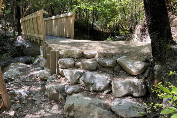 Timber bridge and rock retaining structure built beside a forest stream as part of recreation construction and walking track construction. The image shows civil contractors completing bridge construction, timber structures, erosion control, siteworks and park construction.