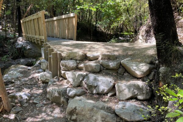 Timber bridge and rock retaining structure built beside a forest stream as part of recreation construction and walking track construction. The image shows civil contractors completing bridge construction, timber structures, erosion control, siteworks and park construction.