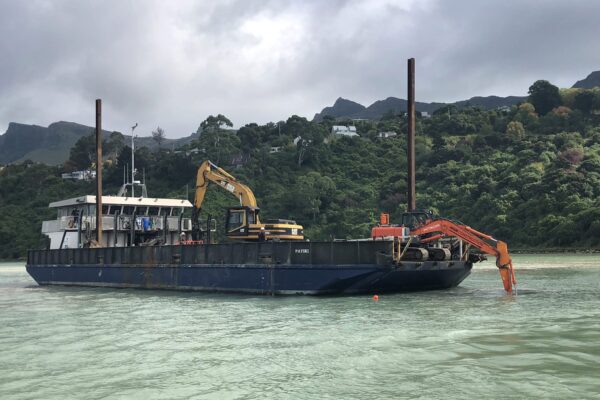 Marine construction barge carrying excavation equipment for civil construction and utility infrastructure works in a harbour environment. The image shows marine services, marine civil contractors, marine barging and coastal construction project management.