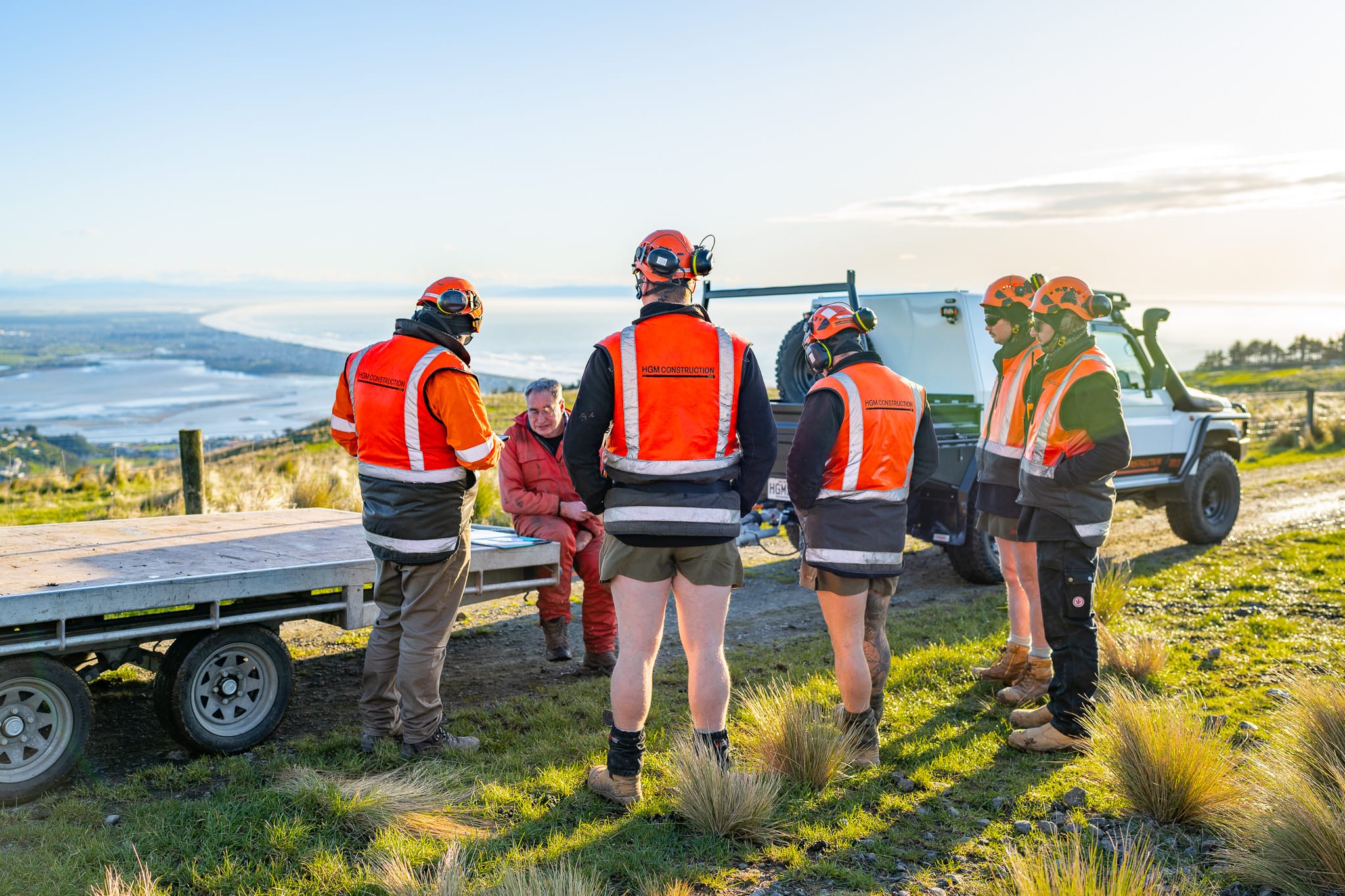 Civil contractors attending a site meeting and briefing beside vehicles and equipment before civil construction works begin. The image shows project management, site preparation, machinery transport, site construction and contractor coordination in a coastal recreation construction setting.